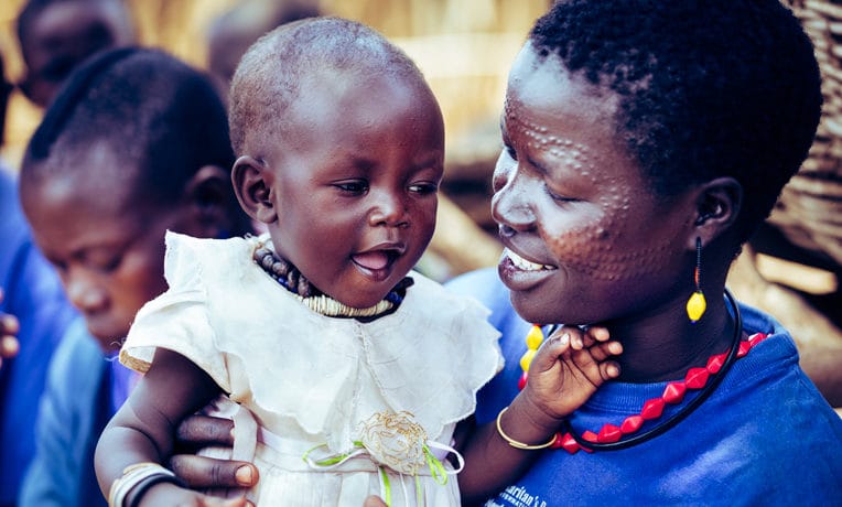 A mother smiling down at the baby she is carrying.