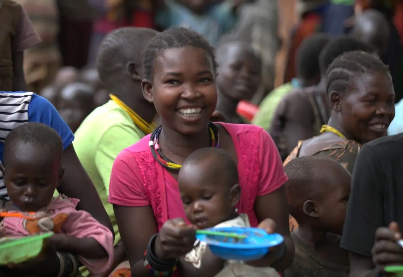 A woman smiling while her child eats from a bowl at a community nutrition class.